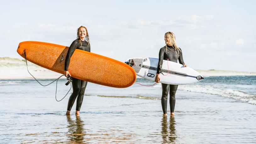 To damer som står i vandkanten med deres surfboards