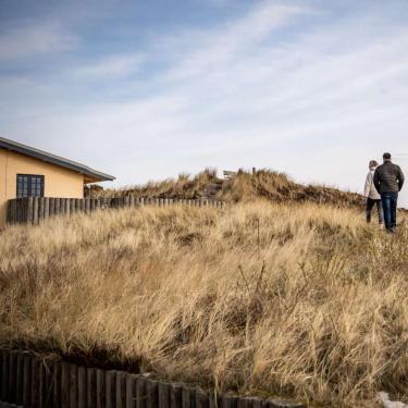 Et par går en tur ved et feriehus i klitlandskab