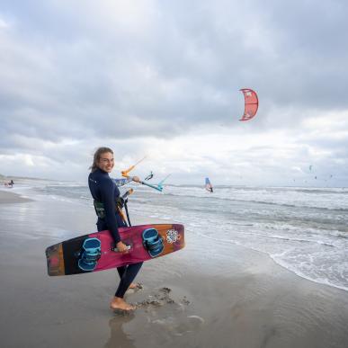 Pige står i strandkanten med kitesurf board
